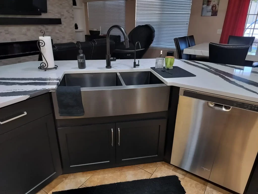 Modern kitchen with a stainless steel farmhouse sink, black faucet, and black cabinetry. The countertop has a white and gray marble design. There is a dishwasher adjacent to the sink, and a Lakeland black kitchen remodel.