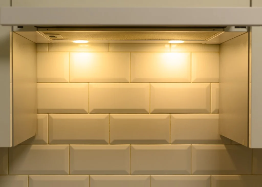 Under-cabinet range hood lights illuminate a cream-colored, glossy subway tile backsplash in a kitchen designed with Aging in Place Renovations for comfort and safety.